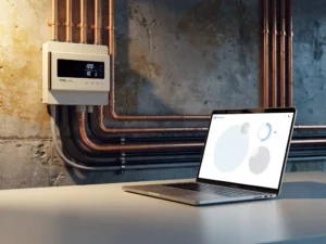 Smart electricity meter on industrial wall connected via copper pipes and cables to a laptop displaying energy billing data.